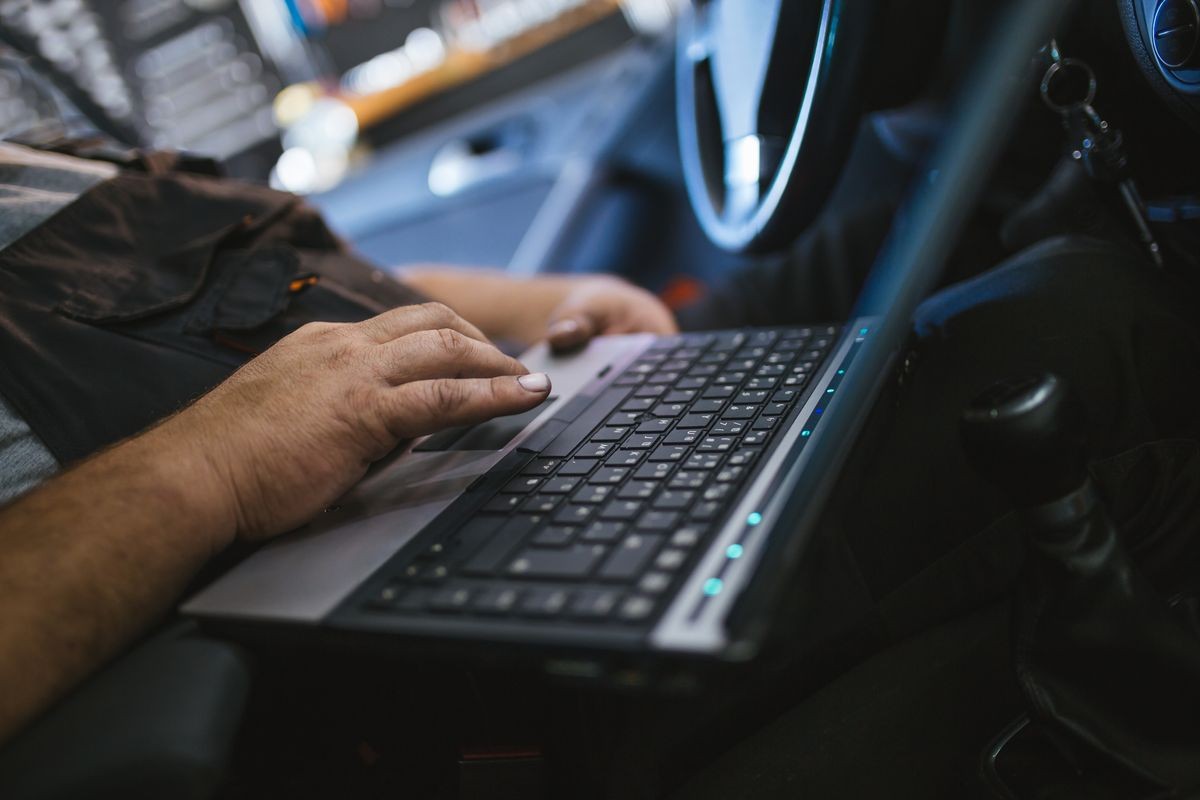 Close up shot of car mechanic using laptop computer for error tracing and diagnostics.